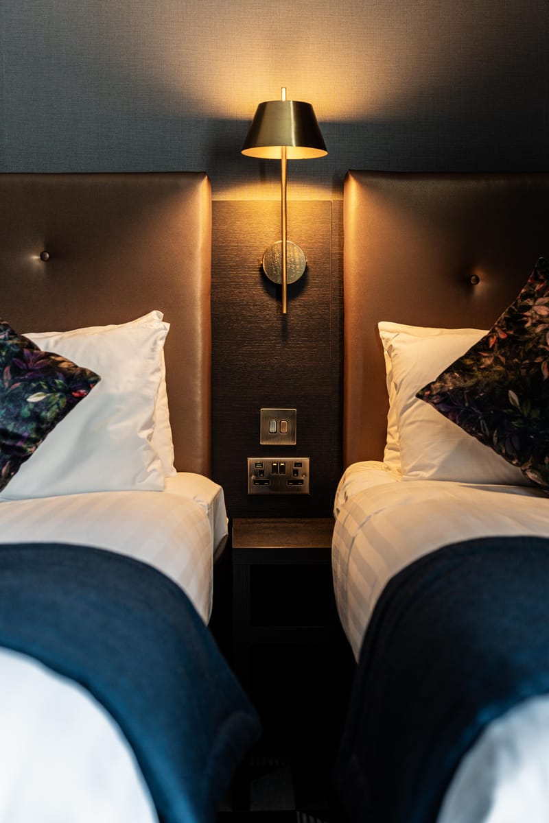 Two beds in a triple room, dressed in white linen with navy runners