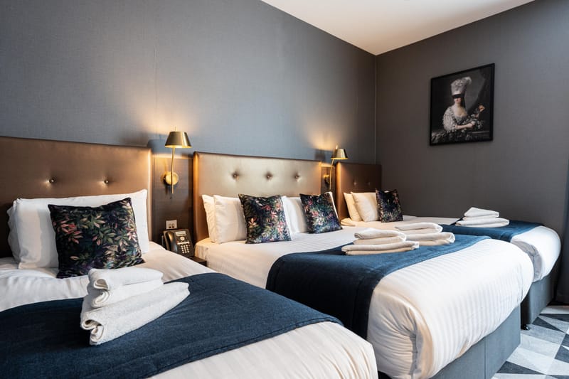 A quadruple room with a double and two single beds beneath framed portraits