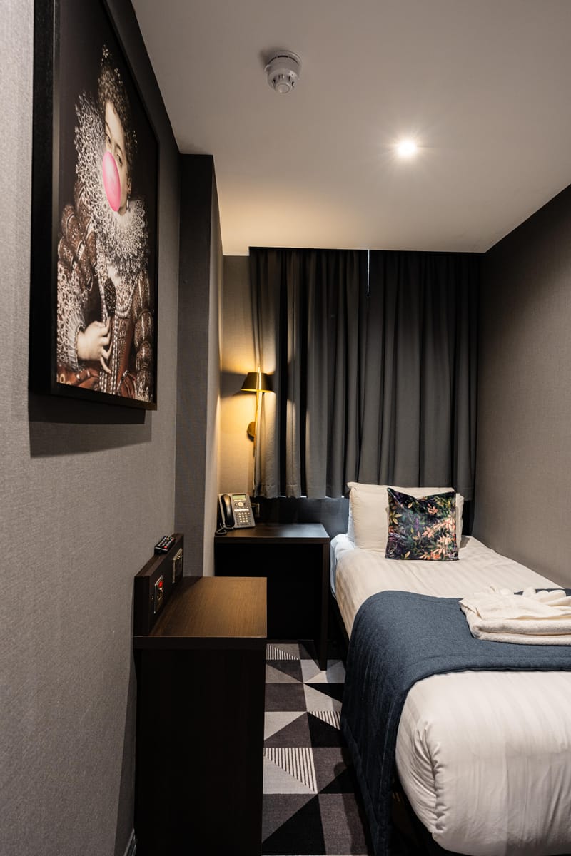 A single room with a botanical velvet cushion, brass reading light and framed artwork