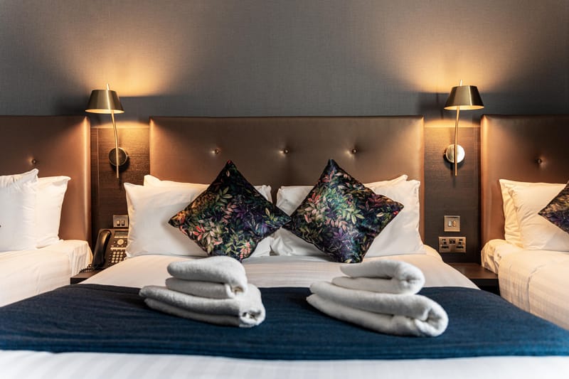 A double bed dressed with towels, framed by two brass reading lights