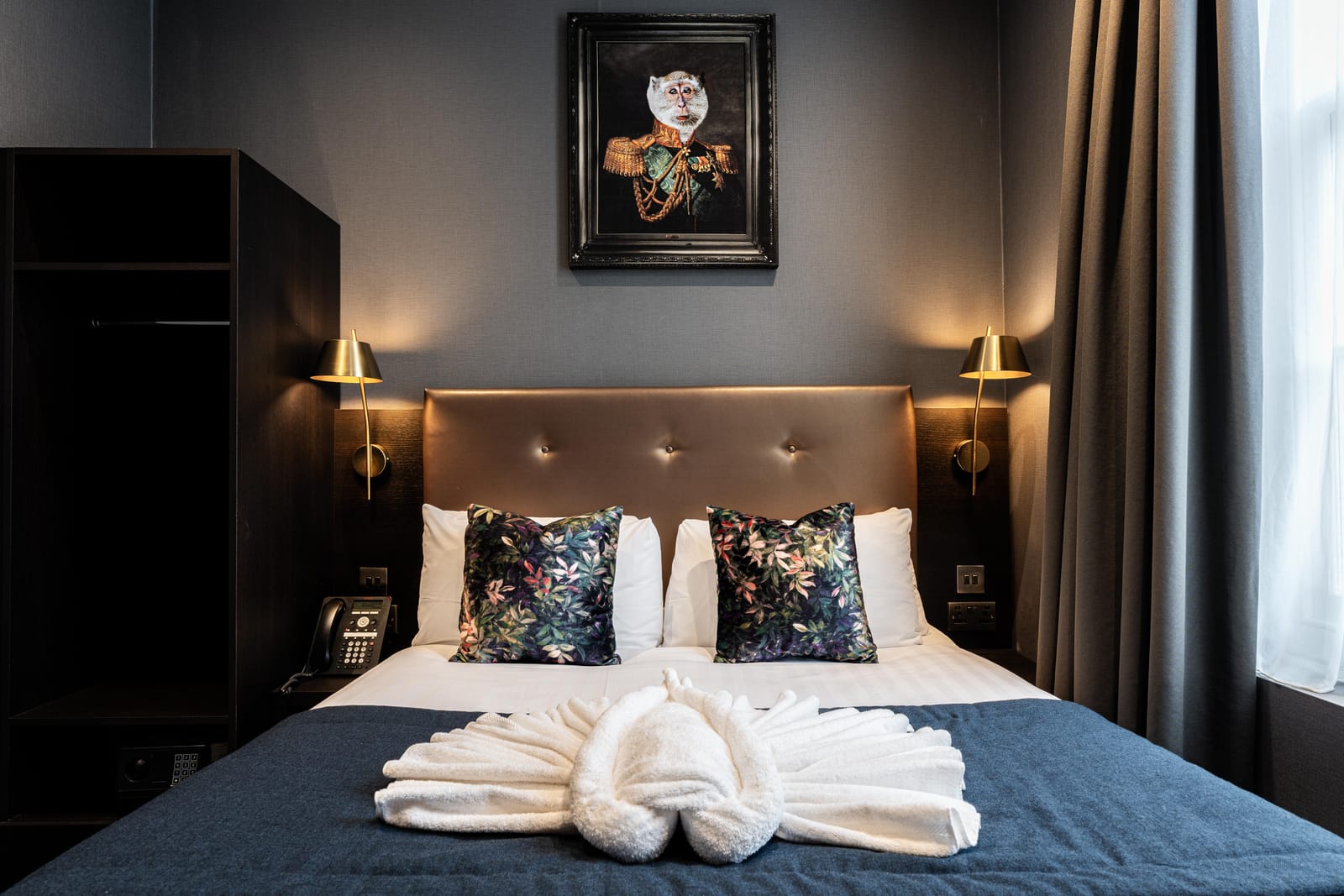 A double room at The House on Warwick — a buttoned leather headboard, brass sconces and a navy runner