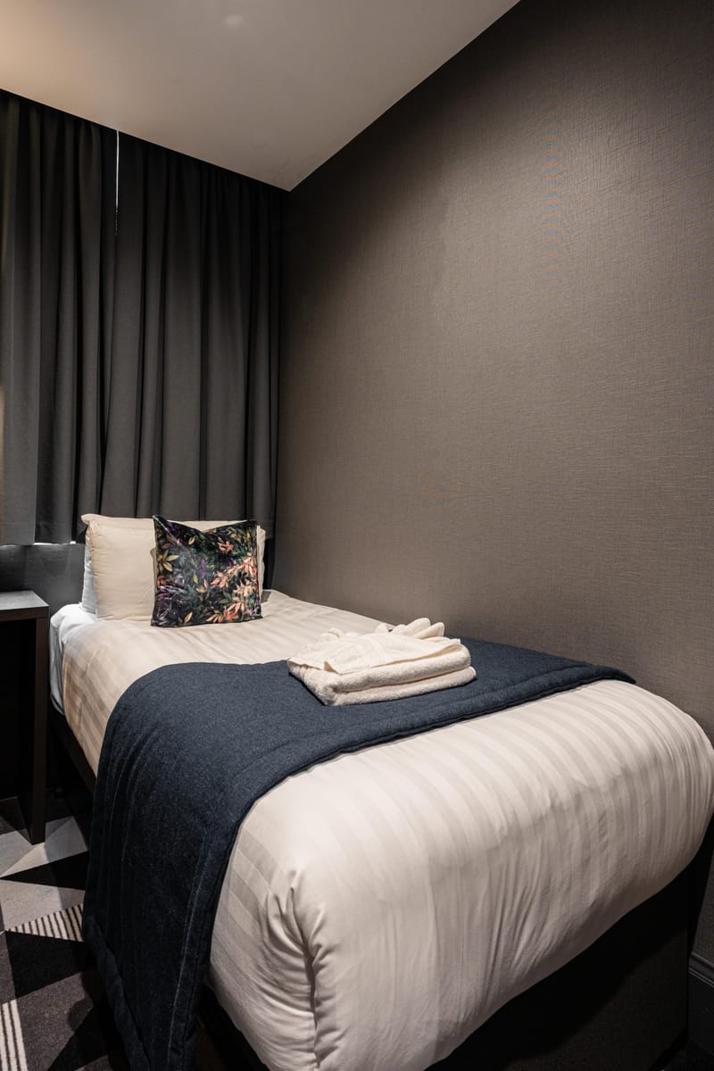 The bed in a single room, dressed in white linen with a navy runner